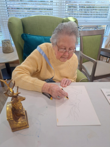 Resident drawing a stag sculpture with coloured pencils, seated in a bright lounge