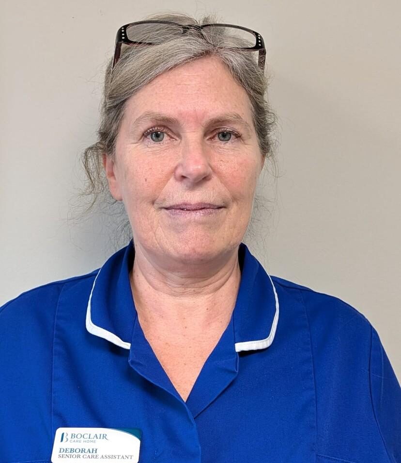care assistant with grey hair tied back in a dark blue nurses uniform