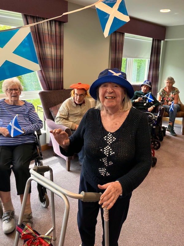 Elderly woman with walker smiling wearing Scotland hat