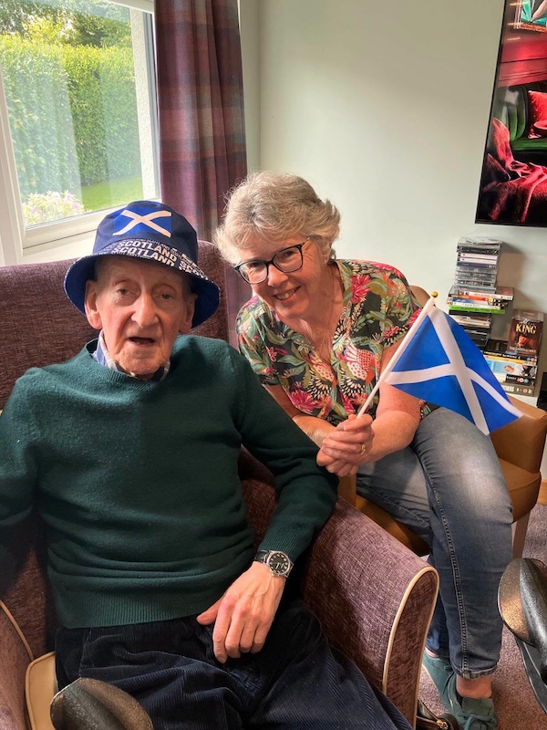 Elderly man and carer sitting smiling with Scotland flags