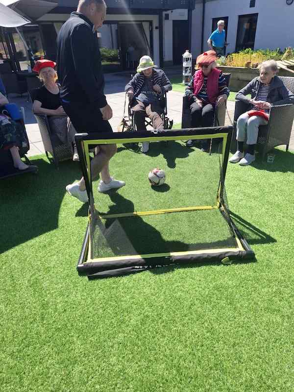Elderly woman in wheelchair kicks football into a goal